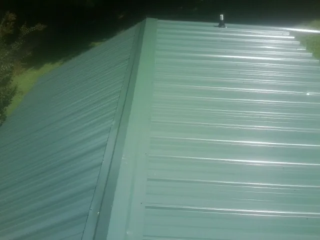 New green metal panels meeting at the ridge of a roof — Flat Roof Repair work by our crew in Lawrenceville