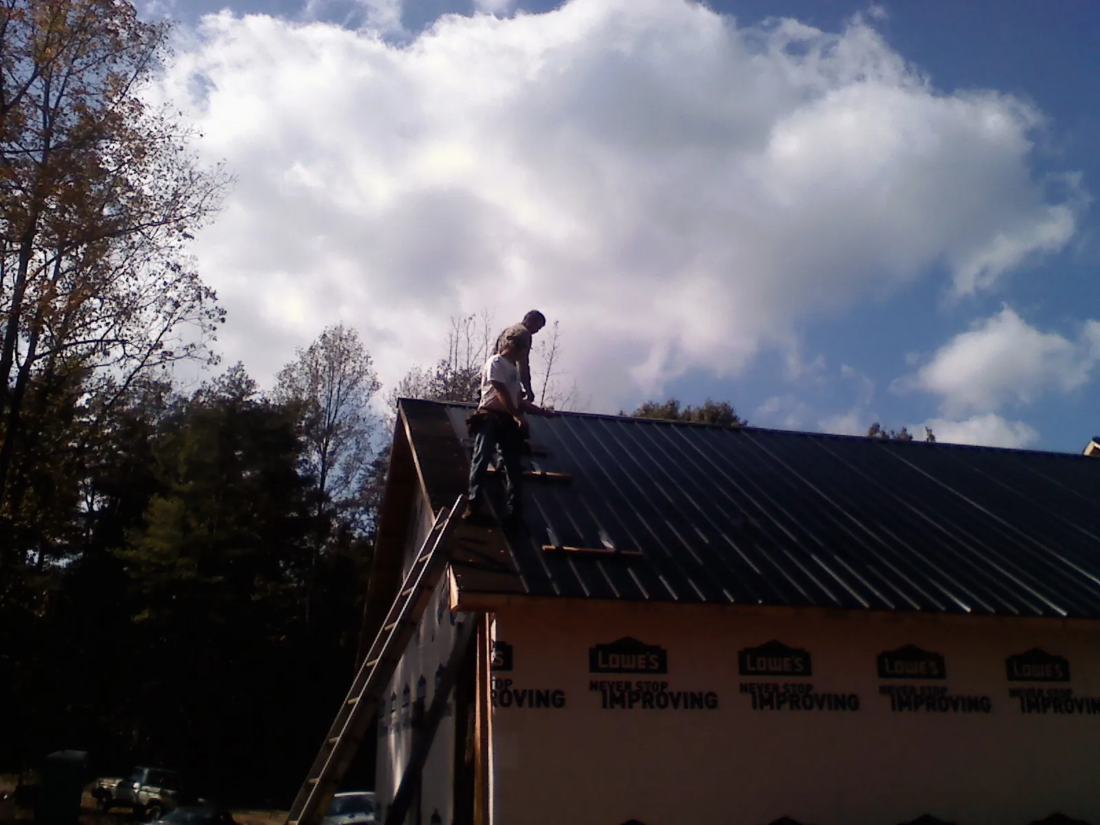 Roofer fastening dark metal panels high against a cloudy sky, from a Roof Inspection job in Lawrenceville