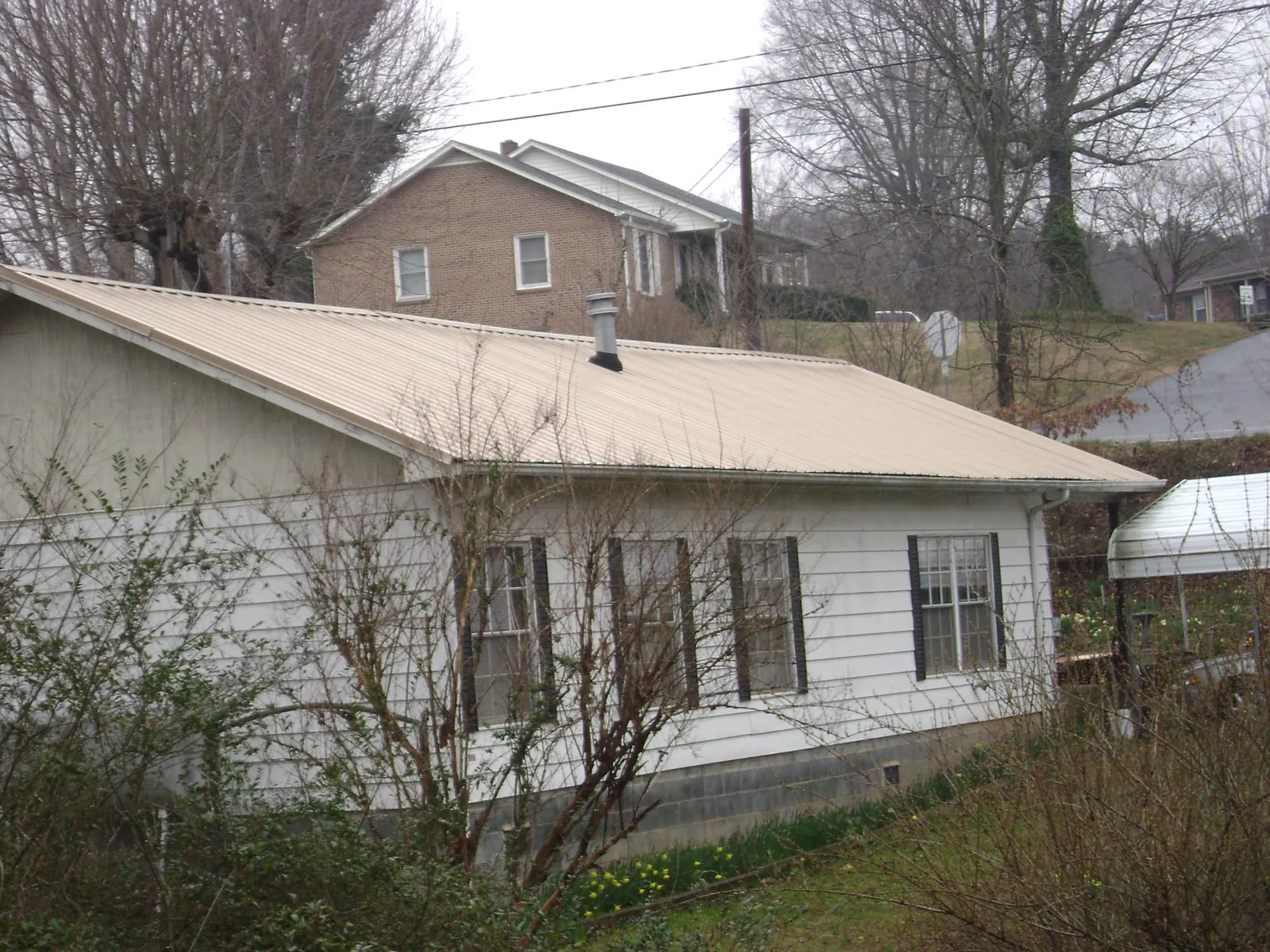 Tan metal roof on a white sided house set into a hillside — Commercial Roofing by Roofing Brothers in Lawrenceville